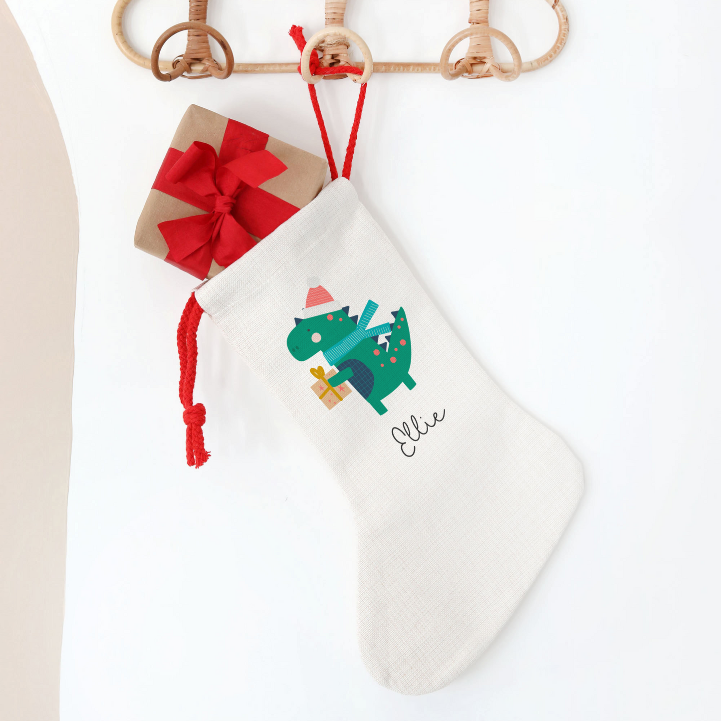 White Christmas stocking with green dinosaur design and red bow on a white background