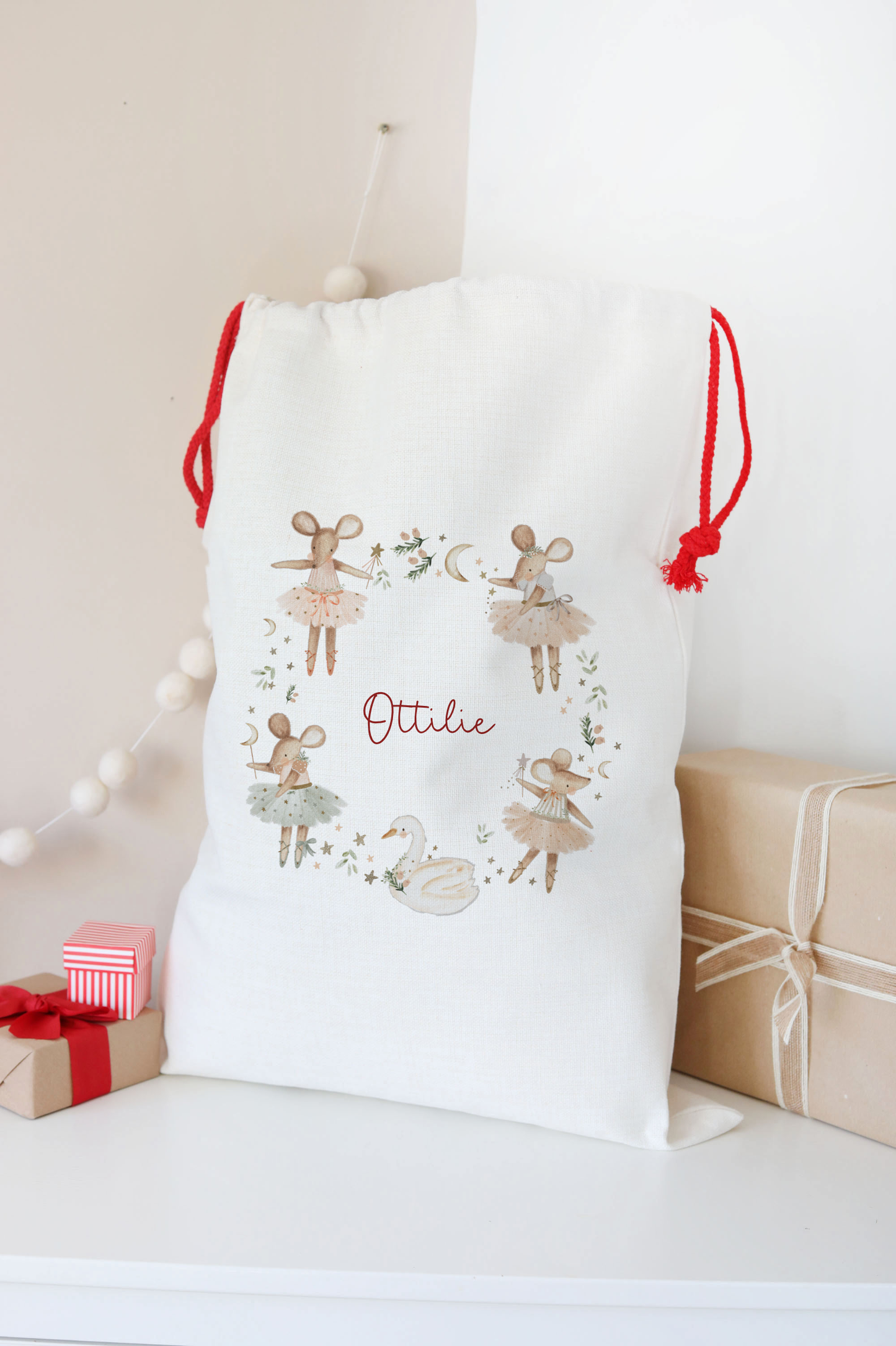 White drawstring bag with decorative elements and 'Ottie' text, placed on a light surface with gift boxes in the background.