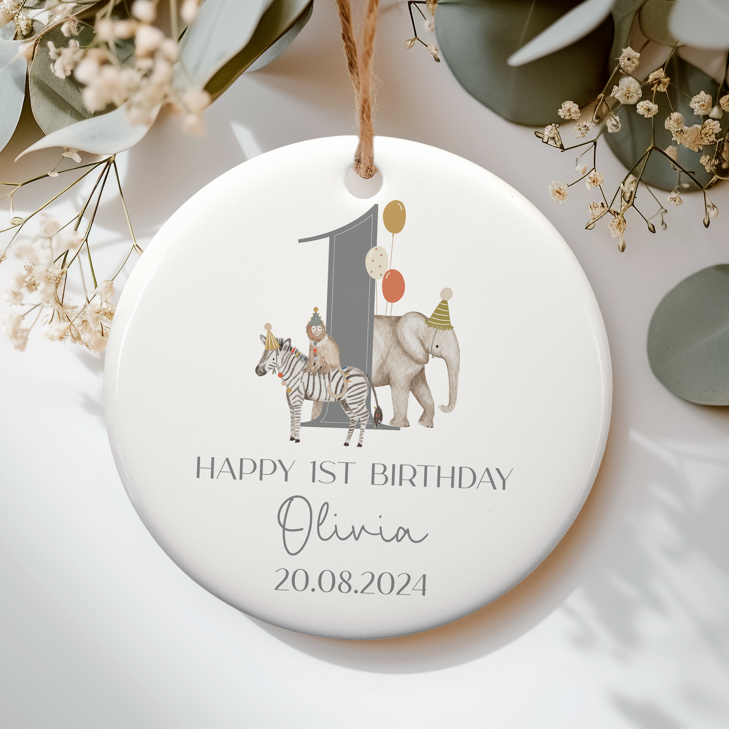 a white ceramic ornament with jungle animals with party hats and balloons around a grey number 1. Text displaying Happy 1st Birthday and personalised with name.