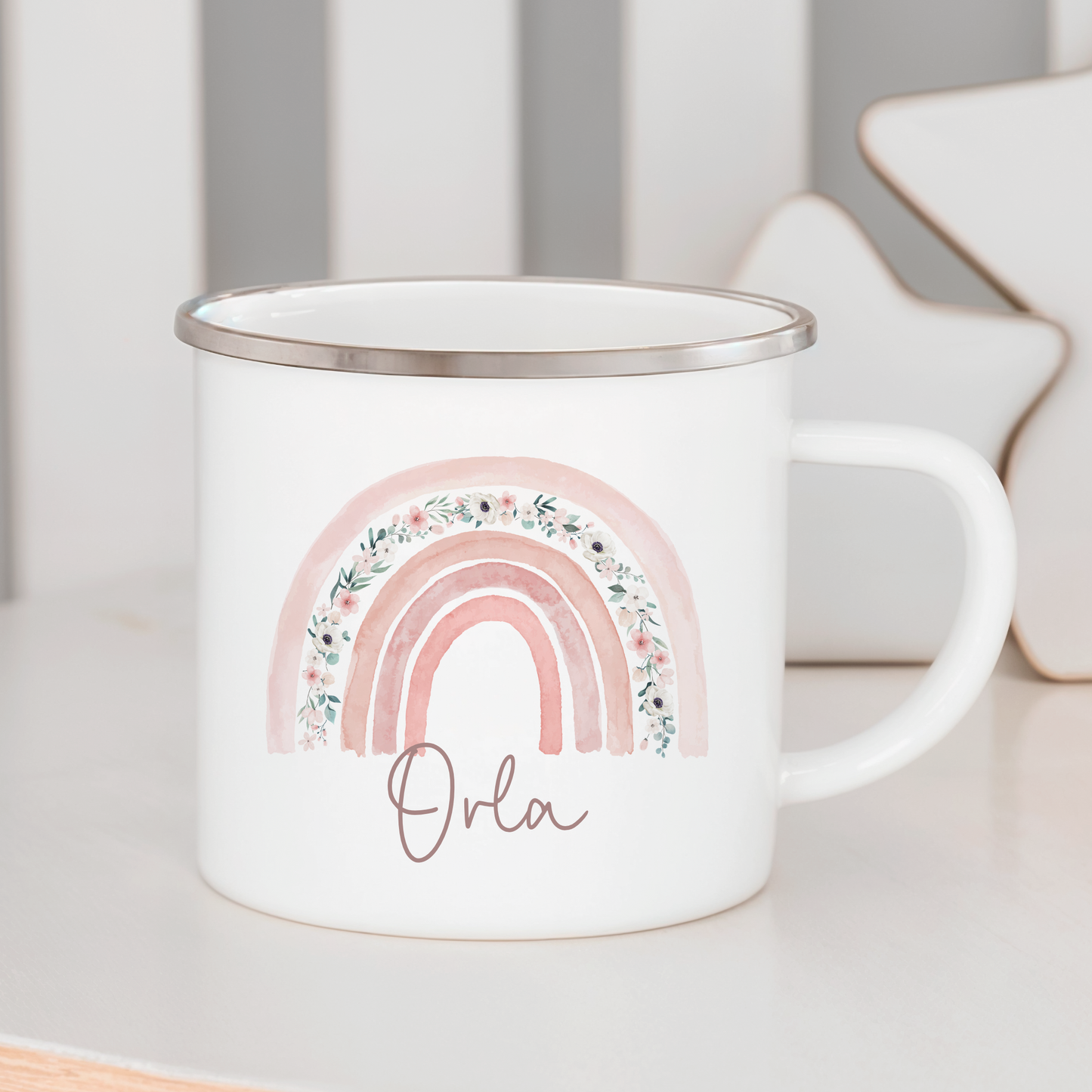 a white enamel mug with a pink floral rainbow, personalised with name