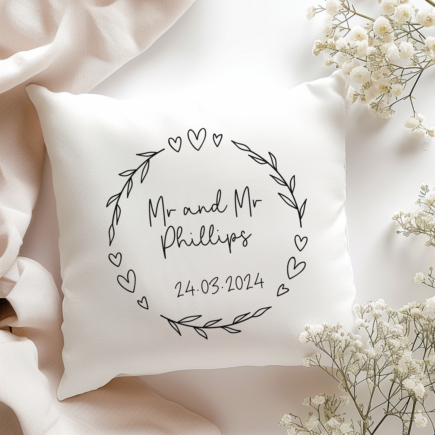 a pillow with a floral heart wreath and personalised with couples name and wedding date in black text.