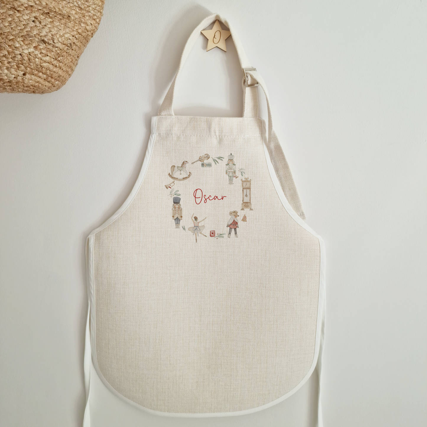 Off white linen like childrens apron with traditional christmas illustrated wreath. Personalised with name in red script font.