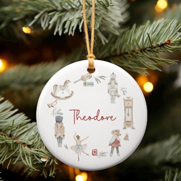 White ceramic ornament with traditional christmas illustrated wreath. Personalised with name in red script font.