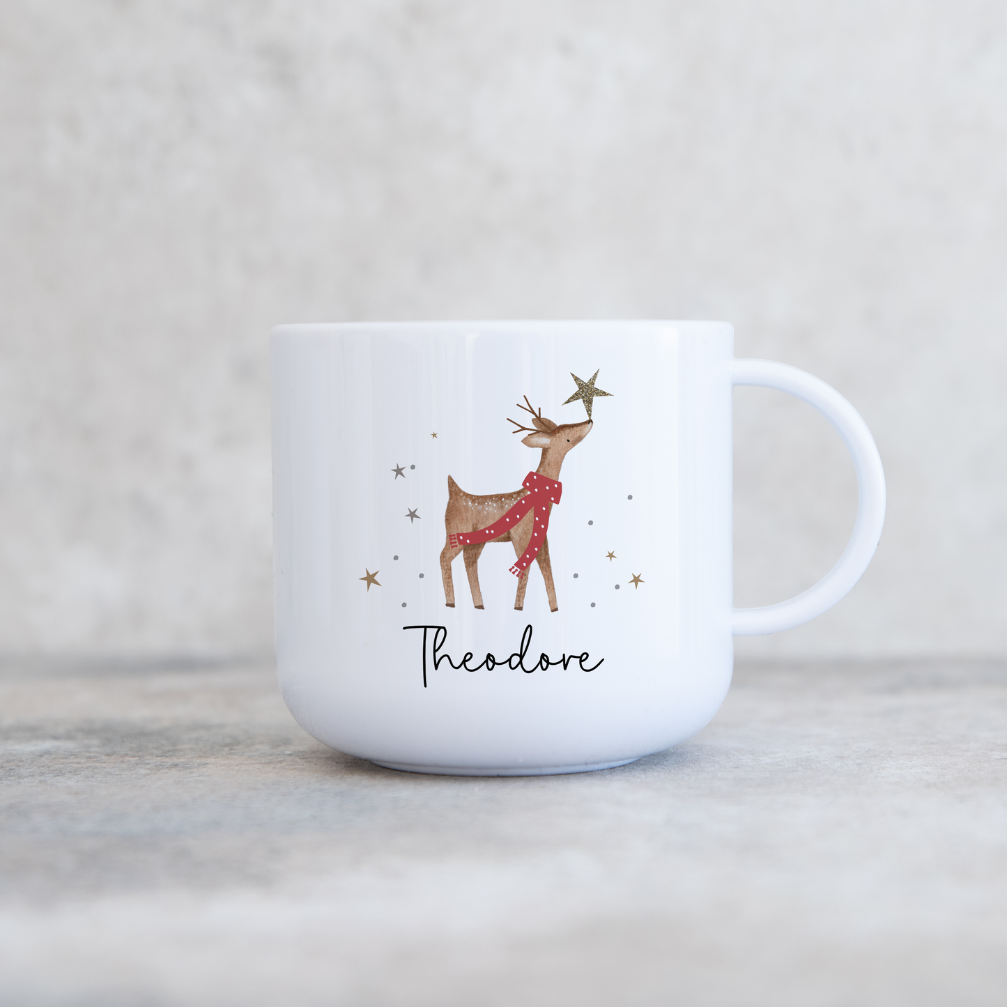 White childrens mug with festive reindeer wearing a red spotty scar f and sparkly star on top of nose. Personalised with name in black script font.