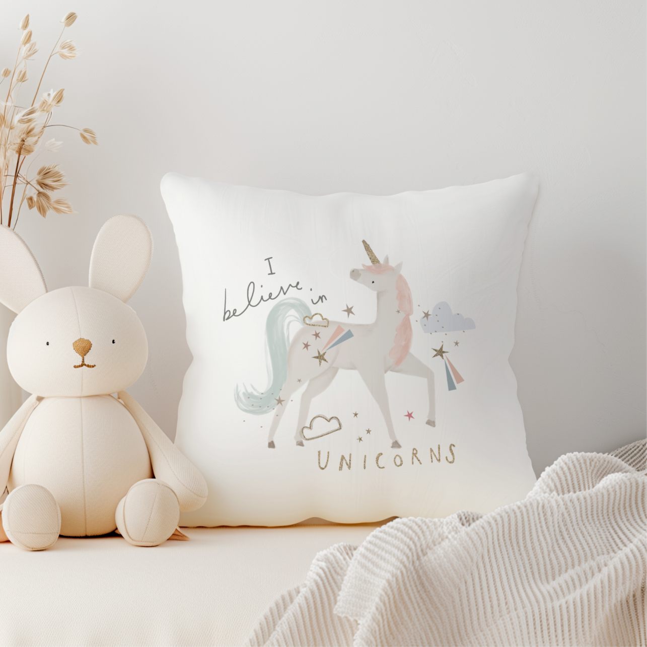 White plush bunny toy next to a pillow with unicorn design on a light gray background