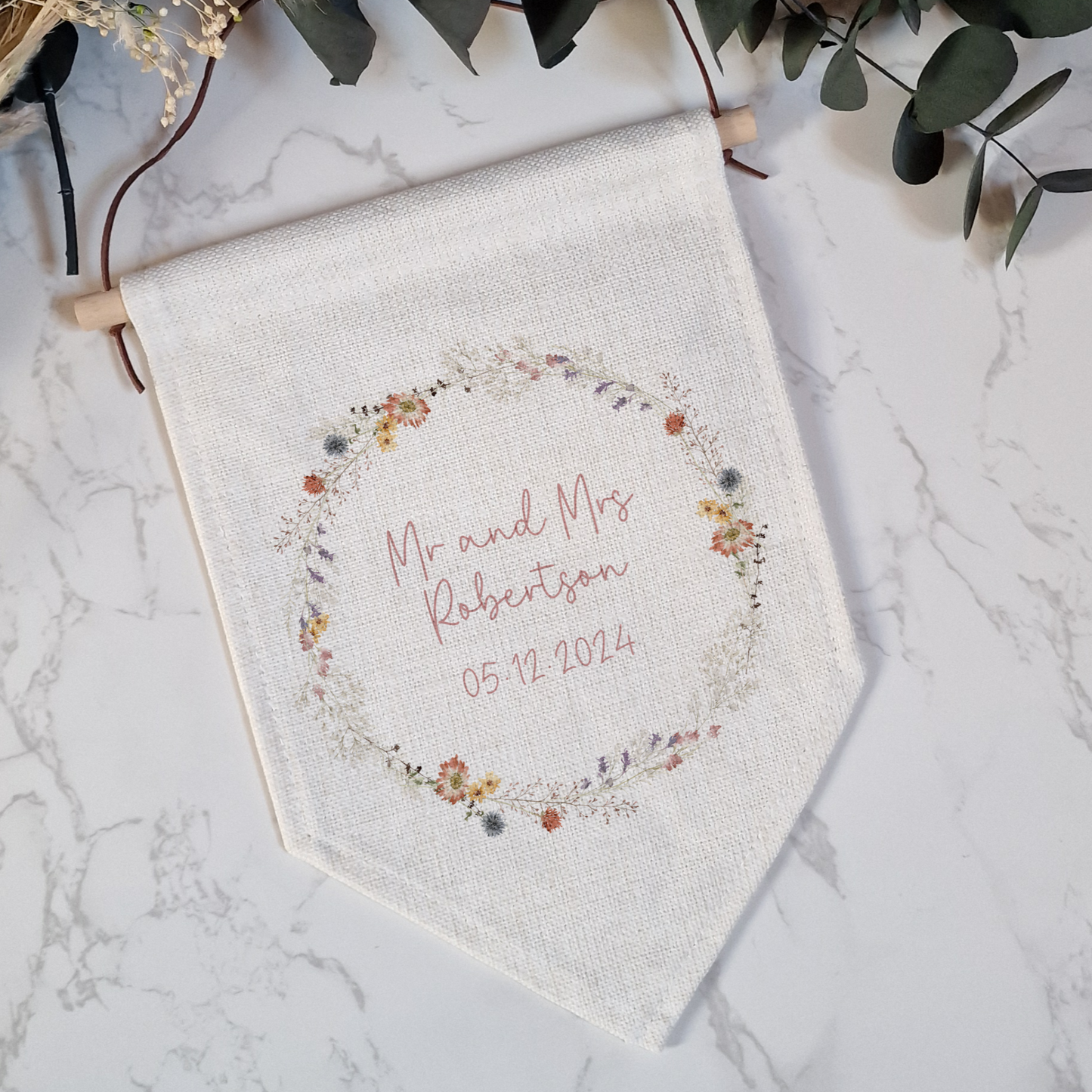 Off white pennant flag with wildflower wreath illustration. Personalised for wedding couple name and wedding date in pink script font.