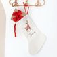 White Christmas stocking with reindeer design hanging on a wooden hanger against a white background.