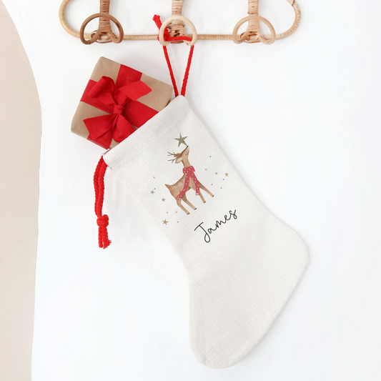 White Christmas stocking with reindeer design hanging on a wooden hanger against a white background.