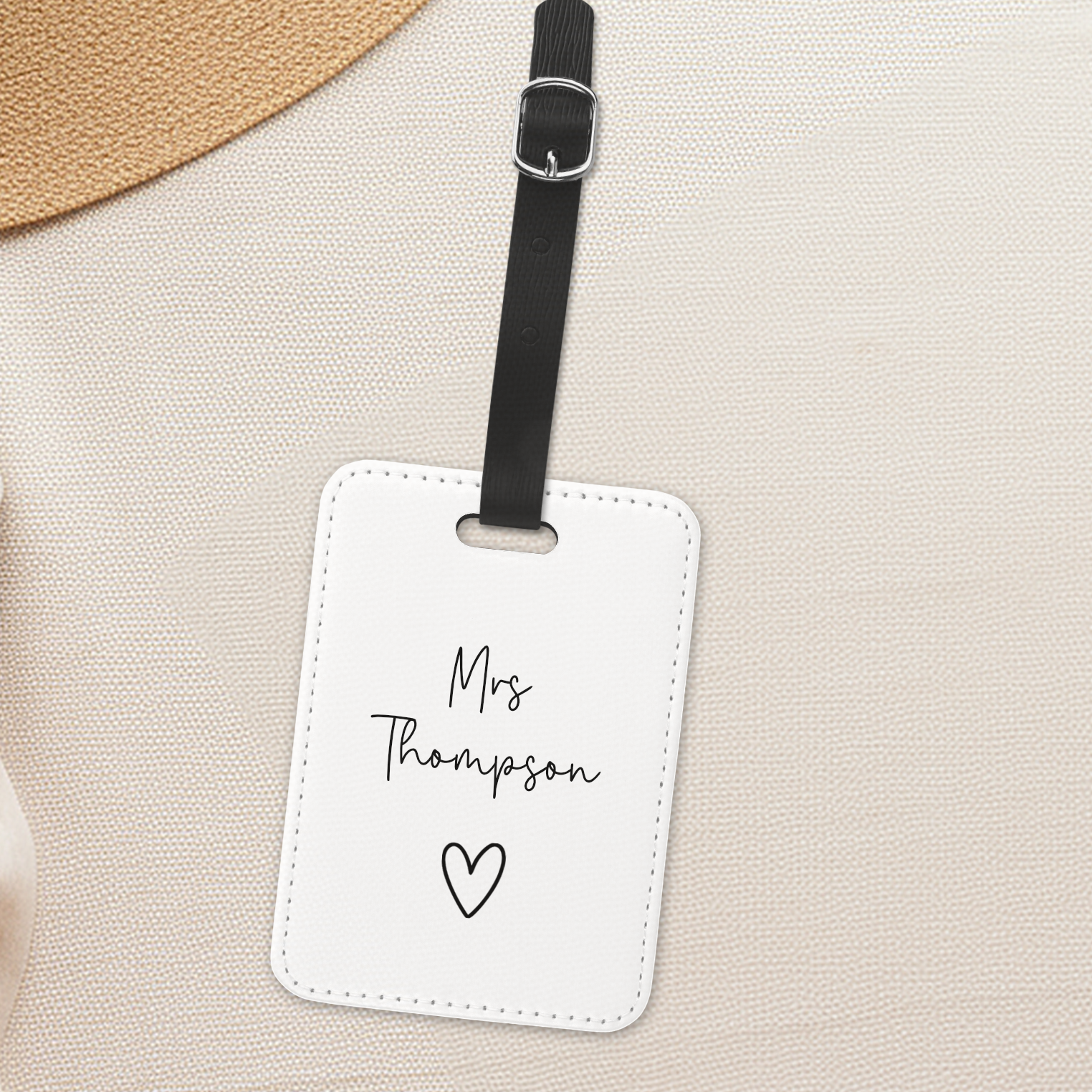 A white luggage tag, with newlyweds name with a heart on it. Black strap on luggage tag.