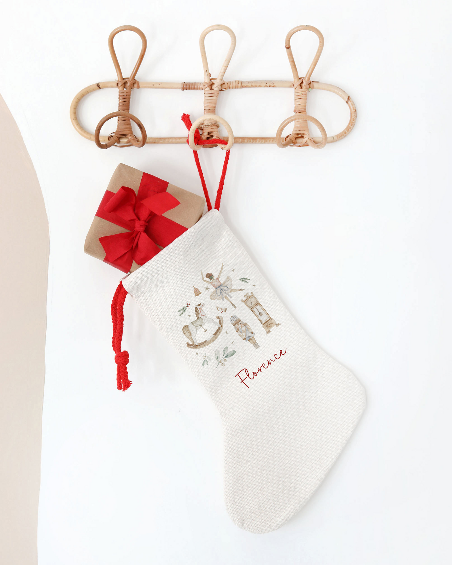 Off white linen stocking hanging on a rattan hook. With double red drawstring. Nutcracker illustration and personalised with the name "Florence".