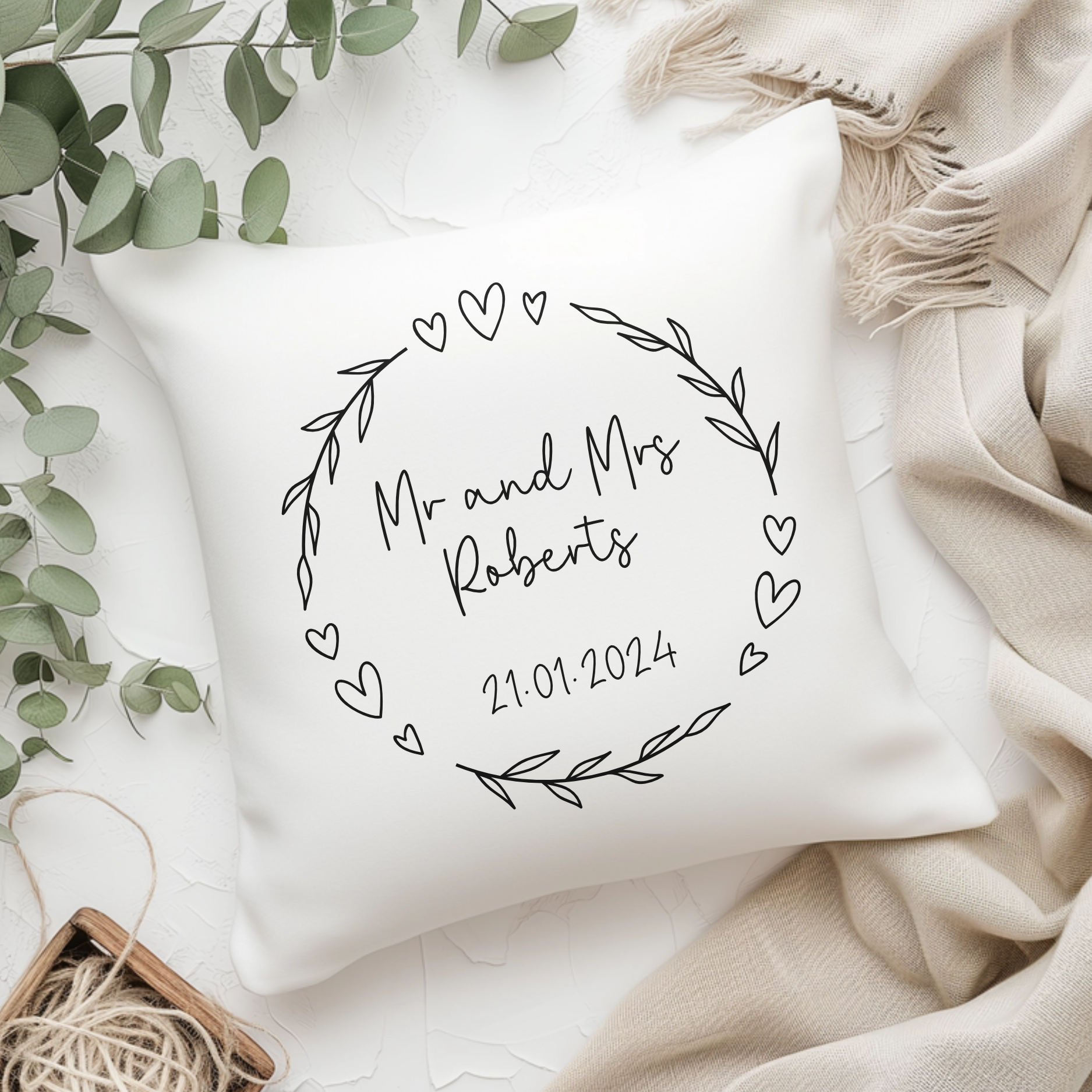 A white pillow personalised with wedding name of mr and mrs including date, with heart and leaf decorative wreath