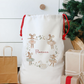 White drawstring bag with decorative elements and 'Florence' text, placed next to Christmas presents and a tree.