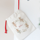 White drawstring bag with reindeer design and 'Feliz' text, hanging on a star-shaped hook.