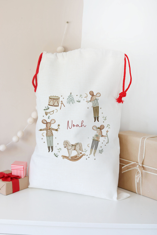 White drawstring bag with illustrations and text, placed on a surface with gift boxes in the background.