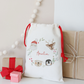 Decorative gift bag with festive characters and 'Amelia' text, surrounded by small gifts on a light background.