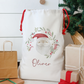 White gift bag with Santa Claus design and 'Oliver' text, surrounded by Christmas presents and decorations.