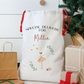 Personalized gift bag with text and graphics, surrounded by Christmas presents and a tree.