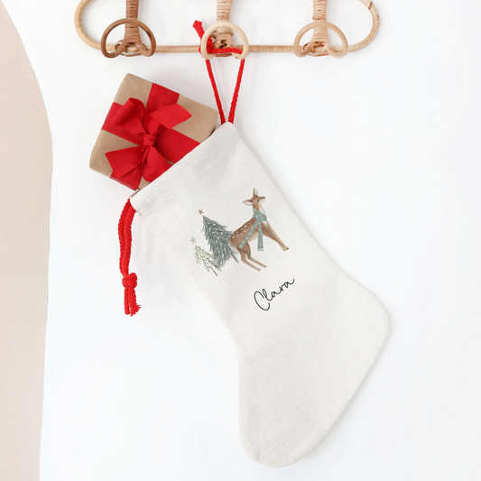 White Christmas stocking with reindeer design, personalised with name. Hanging on a wooden hanger against a white background.