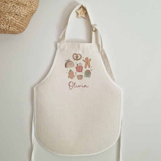 Off white childs apron with christmas treat design, personalised with name in red script font.