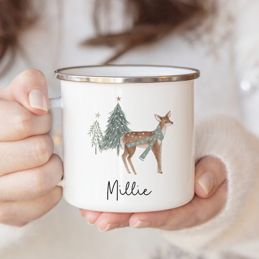 A lady holding a white enamel mug with festive deer and trees illustration, personalised with name in black script font.