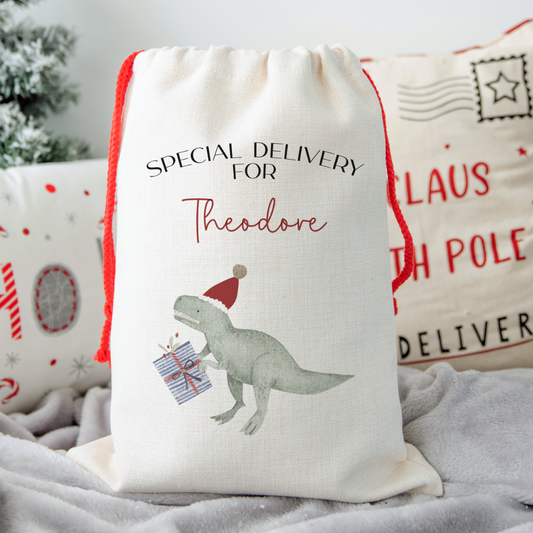 Off white linen santa sack with T-rex carrying a present. Text of special delivery for Theodore