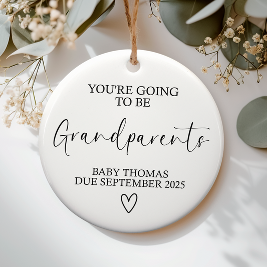 White ceramic ornament with you're going to be grandparents text. Flat lay on a botanical neutral background