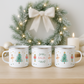 Three Nutcracker-themed mugs on a wooden surface with a decorated wreath in the background.