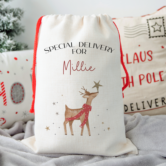 Personalized Christmas sack with reindeer design and text, placed on a soft surface with festive decor.