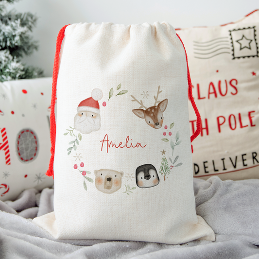 Off white linen sack with illustrated wreath of Santa Claus, Reindeer, Penguin and Polar Bear. Personalised with name in red script font in centre.