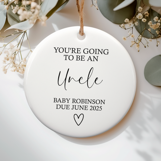 Round ceramic ornament with text about becoming an uncle, surrounded by greenery.