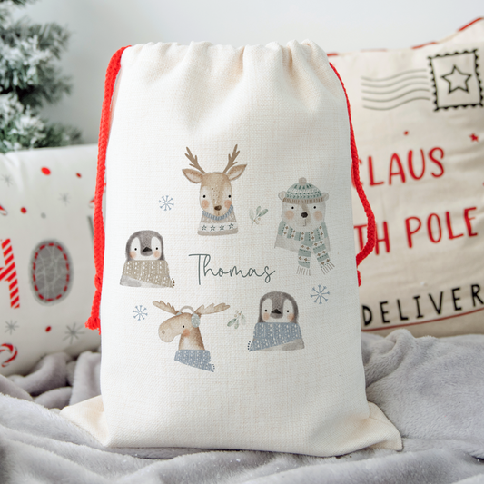 Off white linen santa sack, with red drawstrings on side. Wreath illustration of reindeer, polar bear, penguins and moose with name in the centre.
